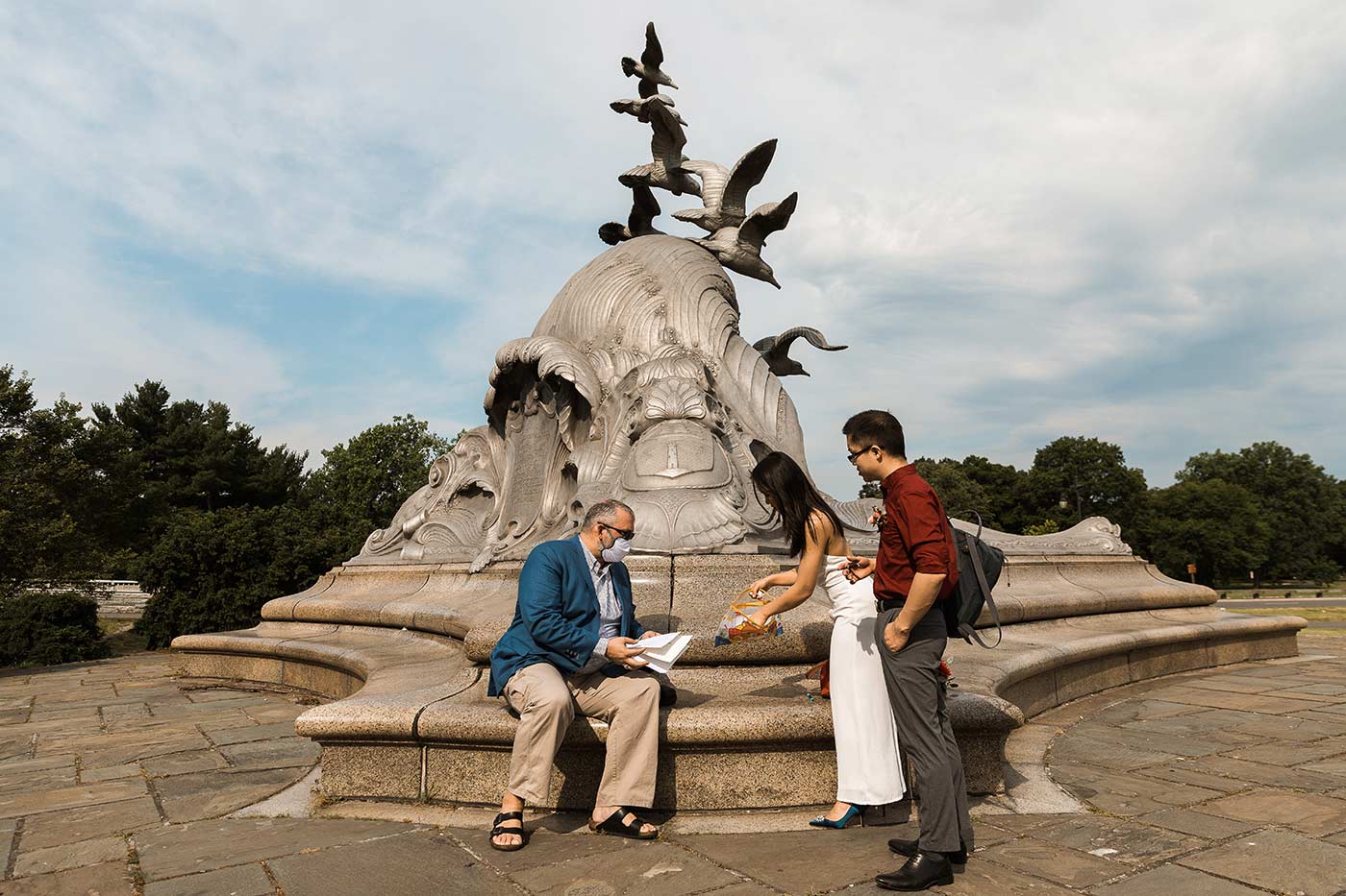 wedding officiant and couple signing marriage certificate in front of navy-merchant marine memorial