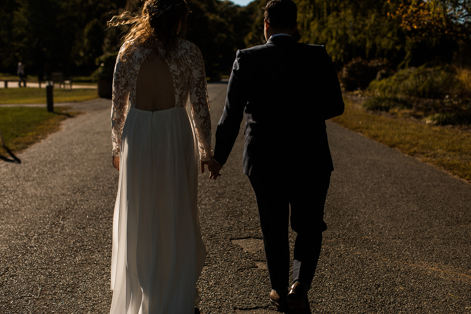 Couple on wedding day holding hands walking down the road during sunset at National Arboretum. 