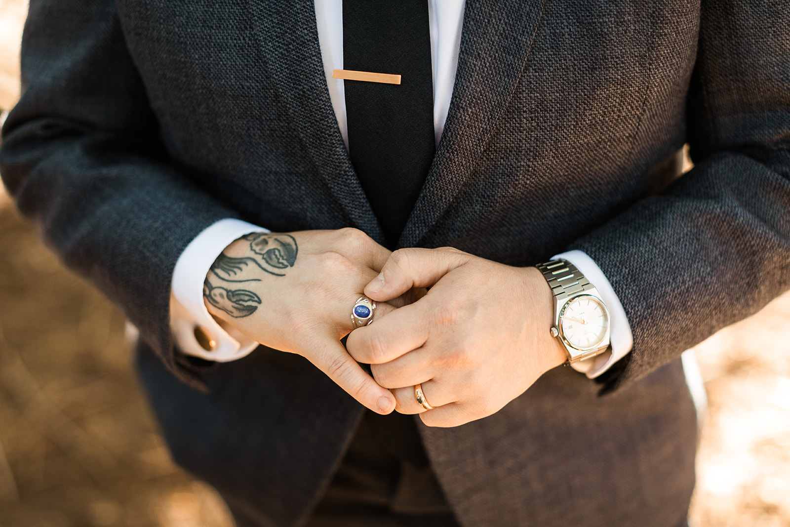 Queer bride wearing suit with lobster hand tattoo, gold rings, and silver watch. 