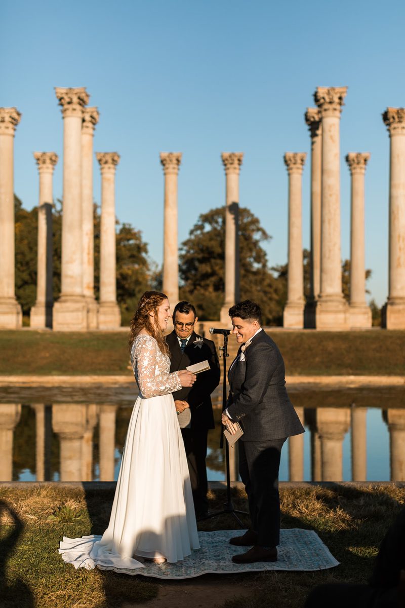 Bride reading her vows to her partner in front of columns at National Arboretum. 