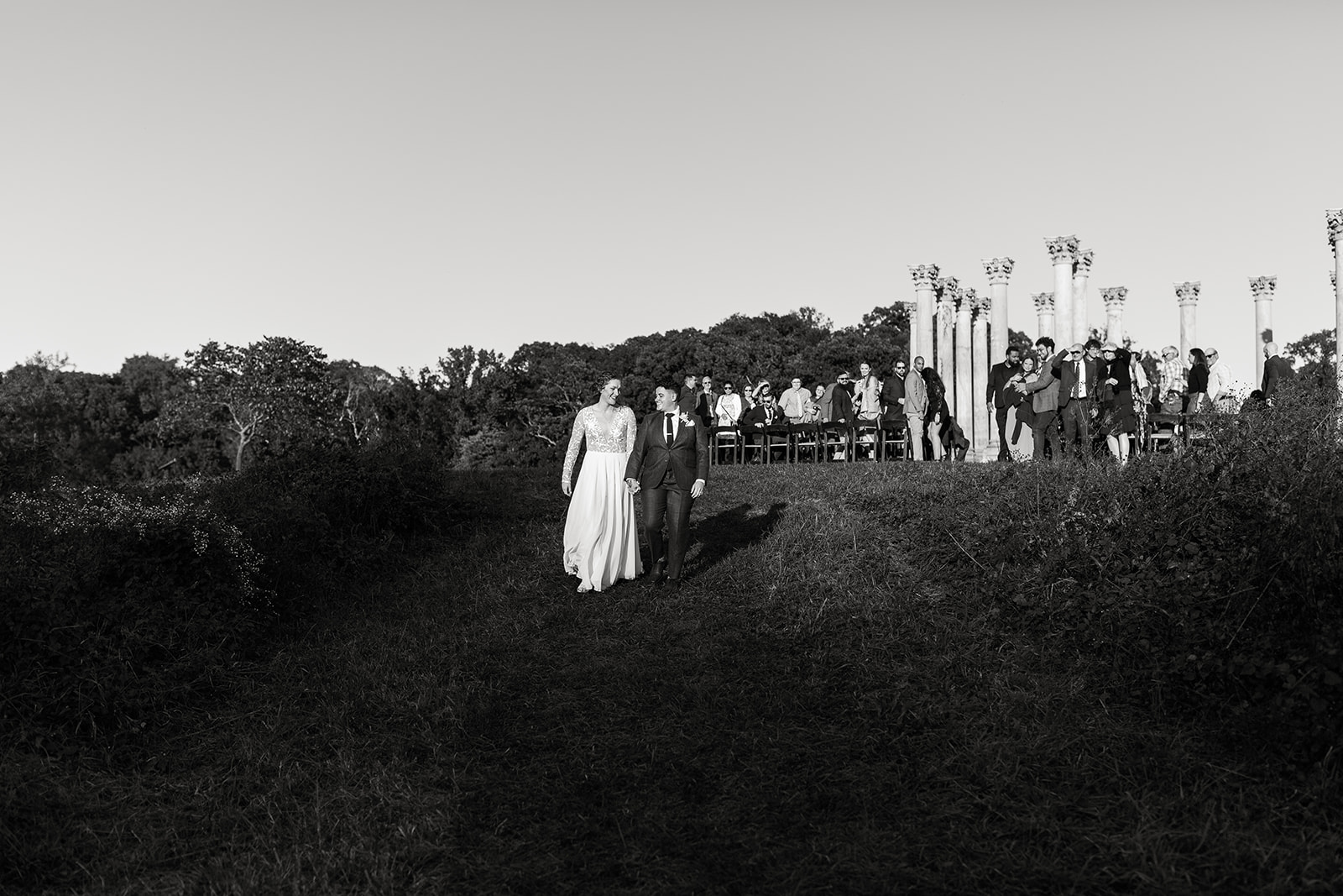 Couple walking away from wedding ceremony holding hands and smiling at National Arboretum. 
