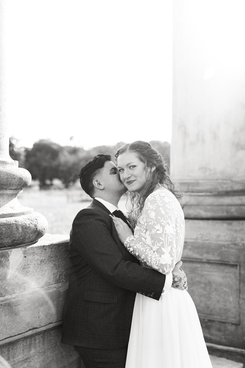 LGBTQ+ couple wearing wedding attire kissing. 