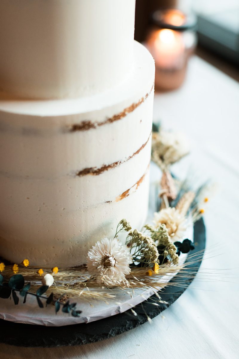Two tier wedding cake with dried flowers around bottom. 