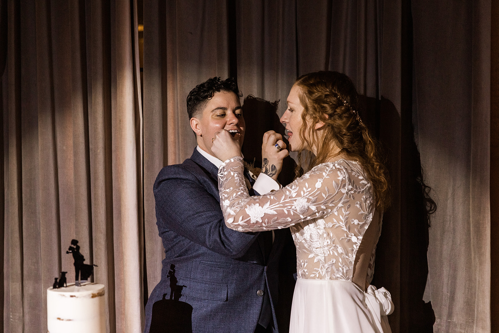 LGBTQ+ couple feeding each other wedding cake. 