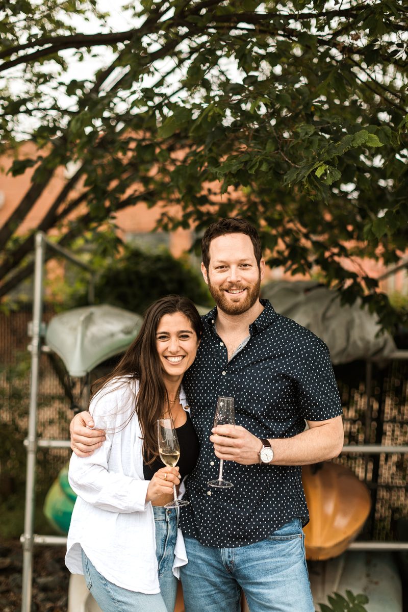 man and woman holding champagne glasses in front of kayaks