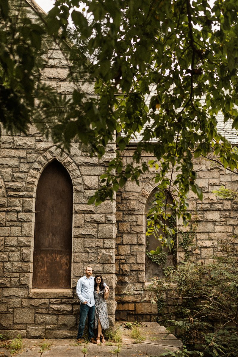 couple standing in front of historic building with stone walls and boarded up windows 