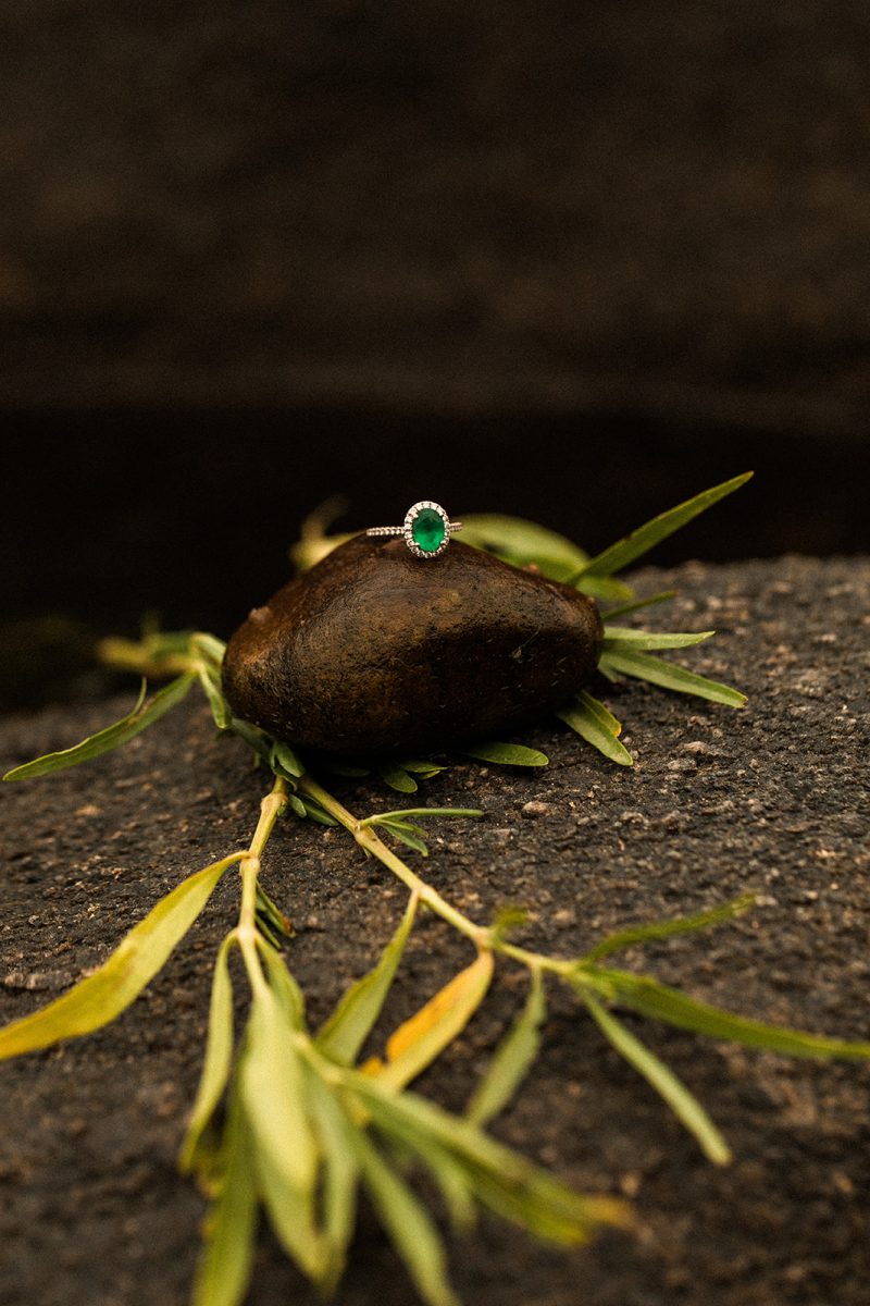 emerald engagement ring with diamond halo sitting on rock 