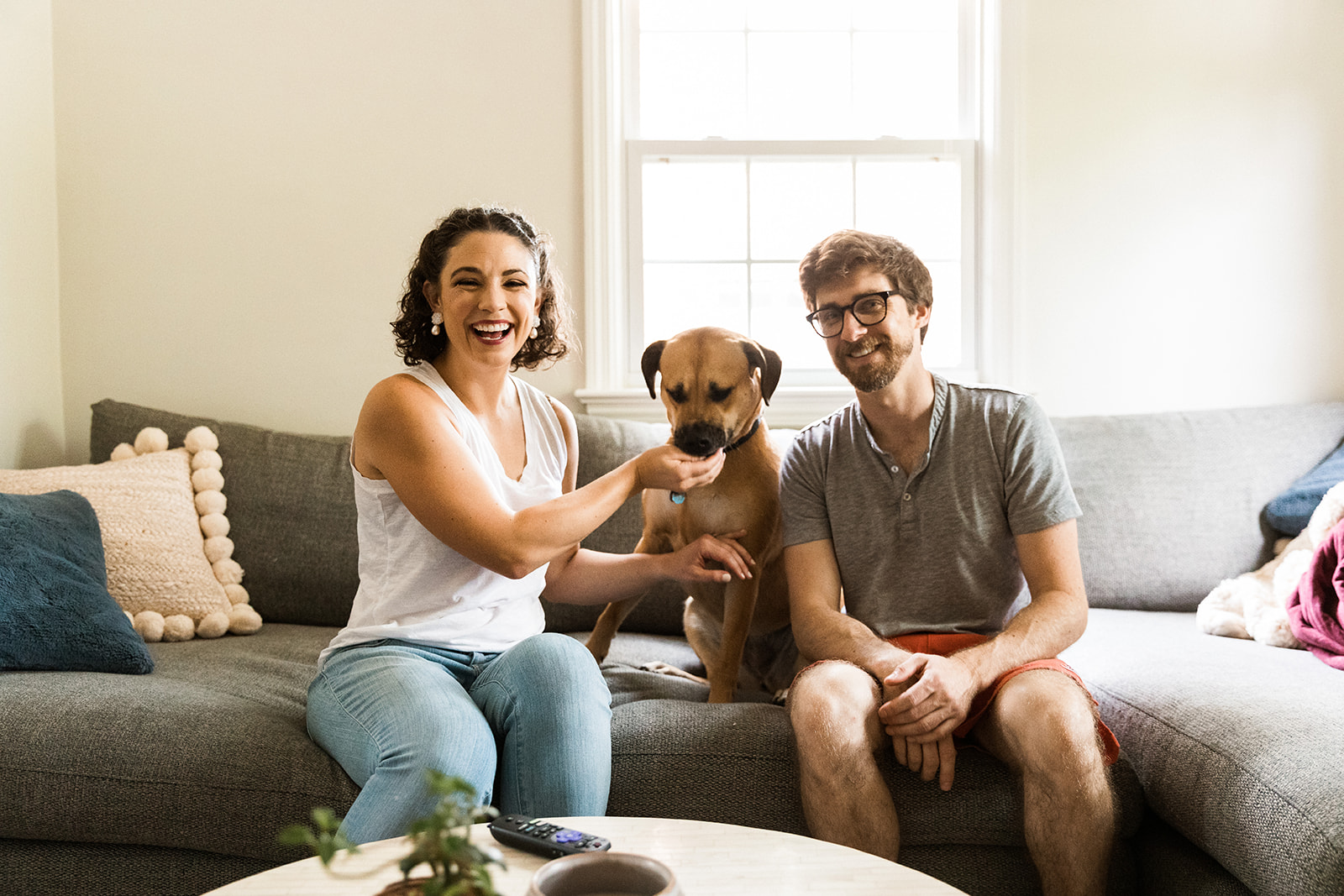 man and woman on couch with brown dog sitting between them 