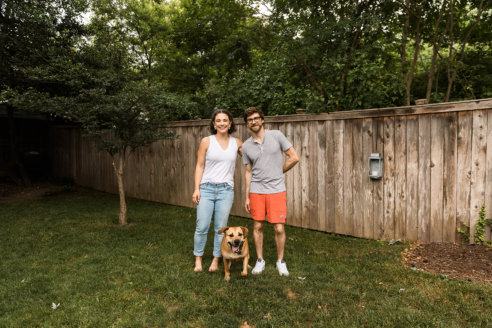 man and woman standing in yard with brown dog between them