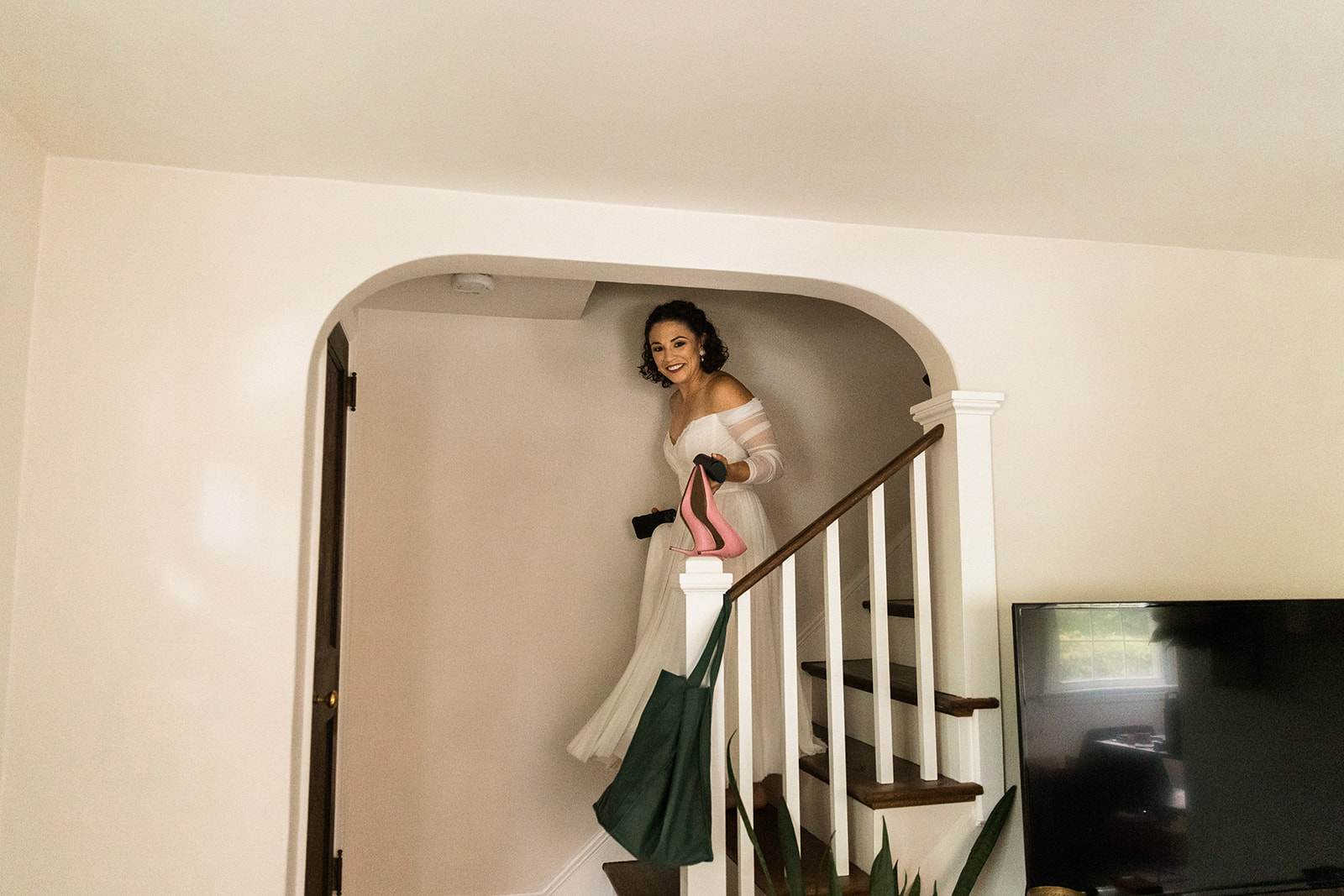bride coming down stairs in her house holding pink heels