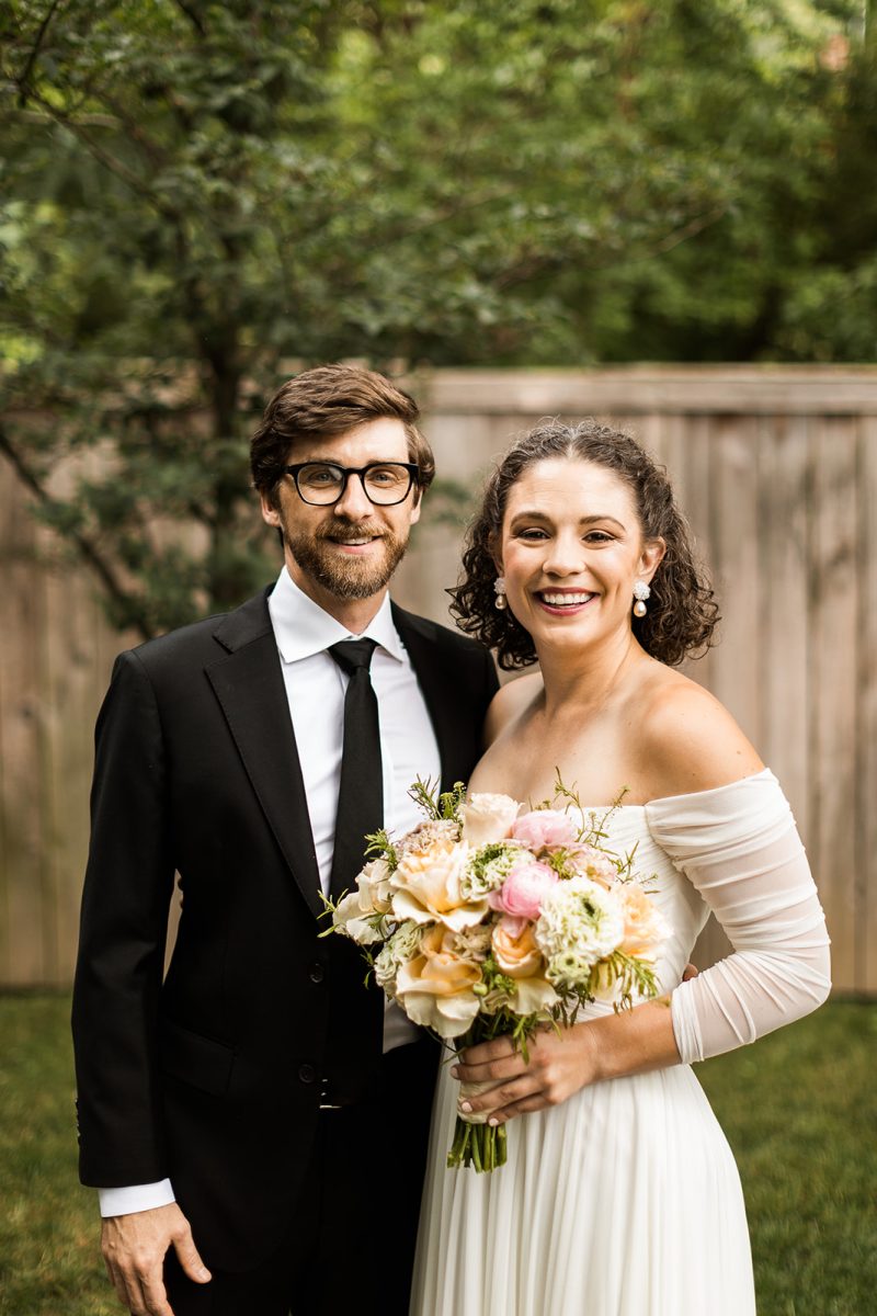 Groom wearing black suit and bride wearing off-the-shoulder cream gown and holding pink and blush bouquet