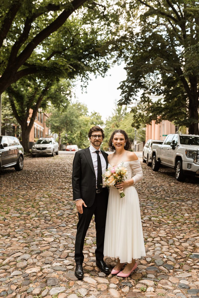 bride and groom standing in the middle of a cobblestone road in old town alexandria 