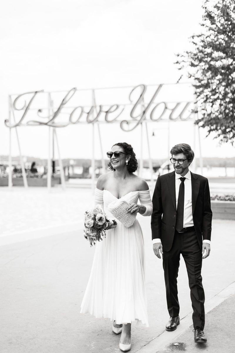 groom and bride wearing sunglasses walking with "I love you" sign in the background