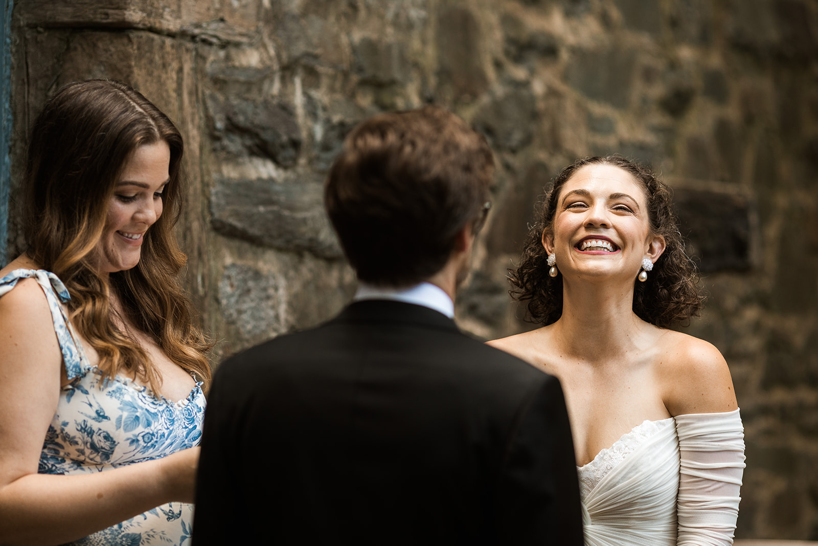 bride laughing during wedding ceremony in front of the stone wall in the garden at carlyle house