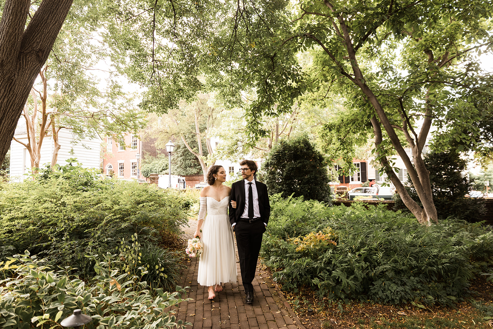 bride and groom walking arm in arm through the gardens at carlyle house in alexandria virginia