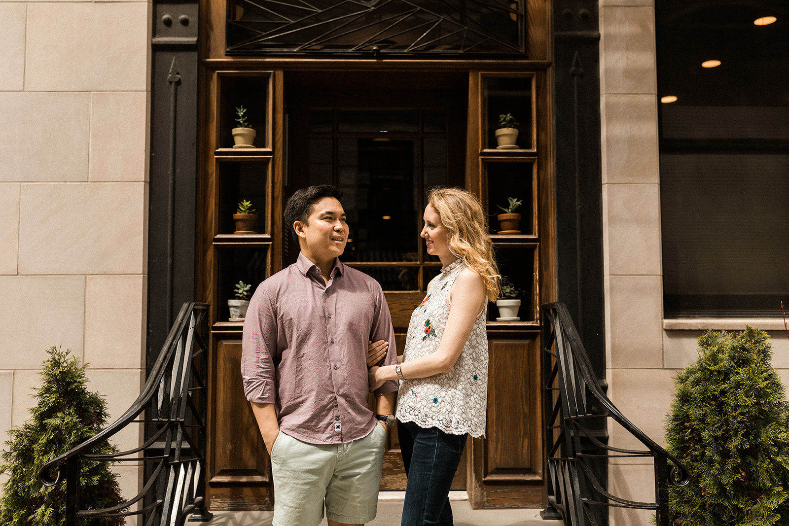 woman holding man's arm while standing in front of unique wooden doorway with potted plants