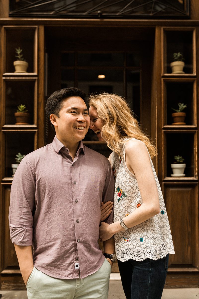 woman and man laughing with wooden doorway and potted plants in background
