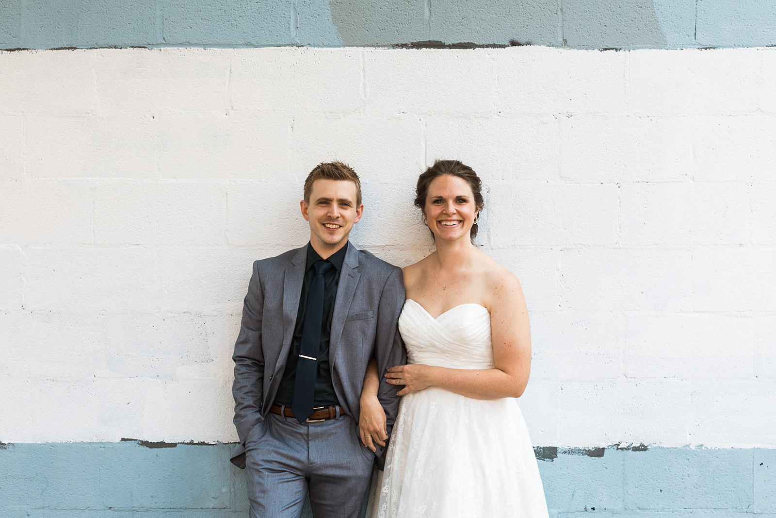 bride and groom posing in front of brick wall painted blue and white
