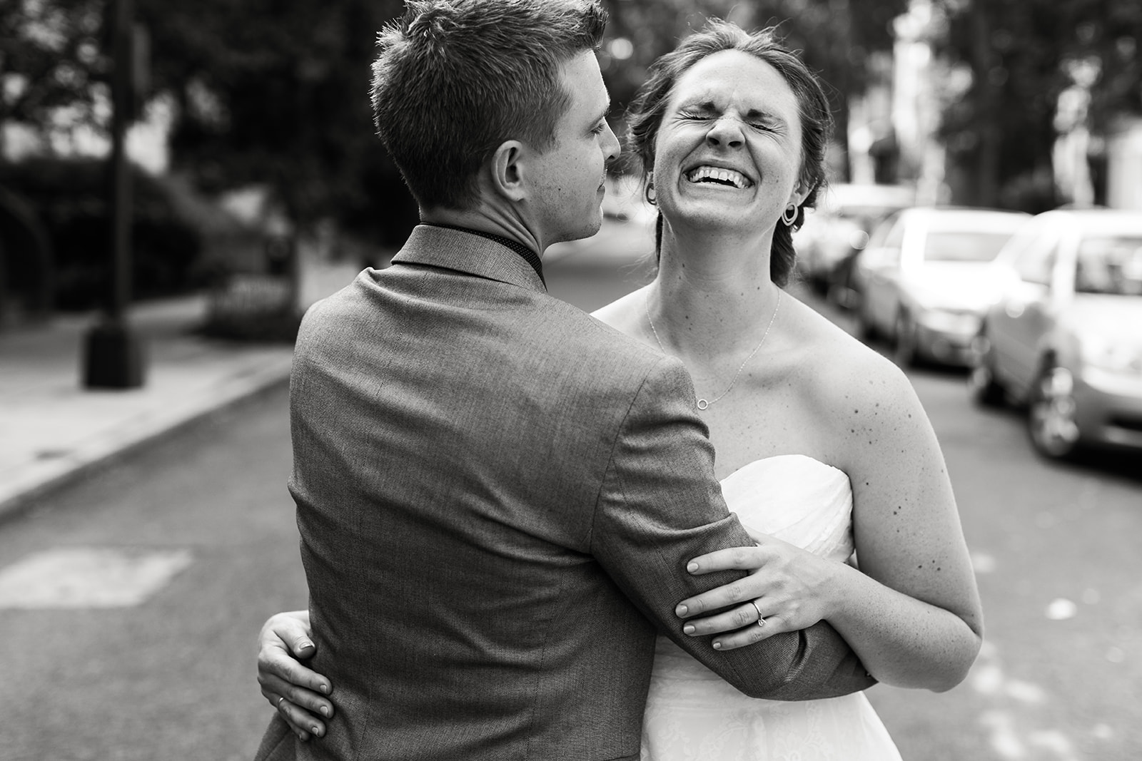 black and white photo of bride laughing while hugging groom 